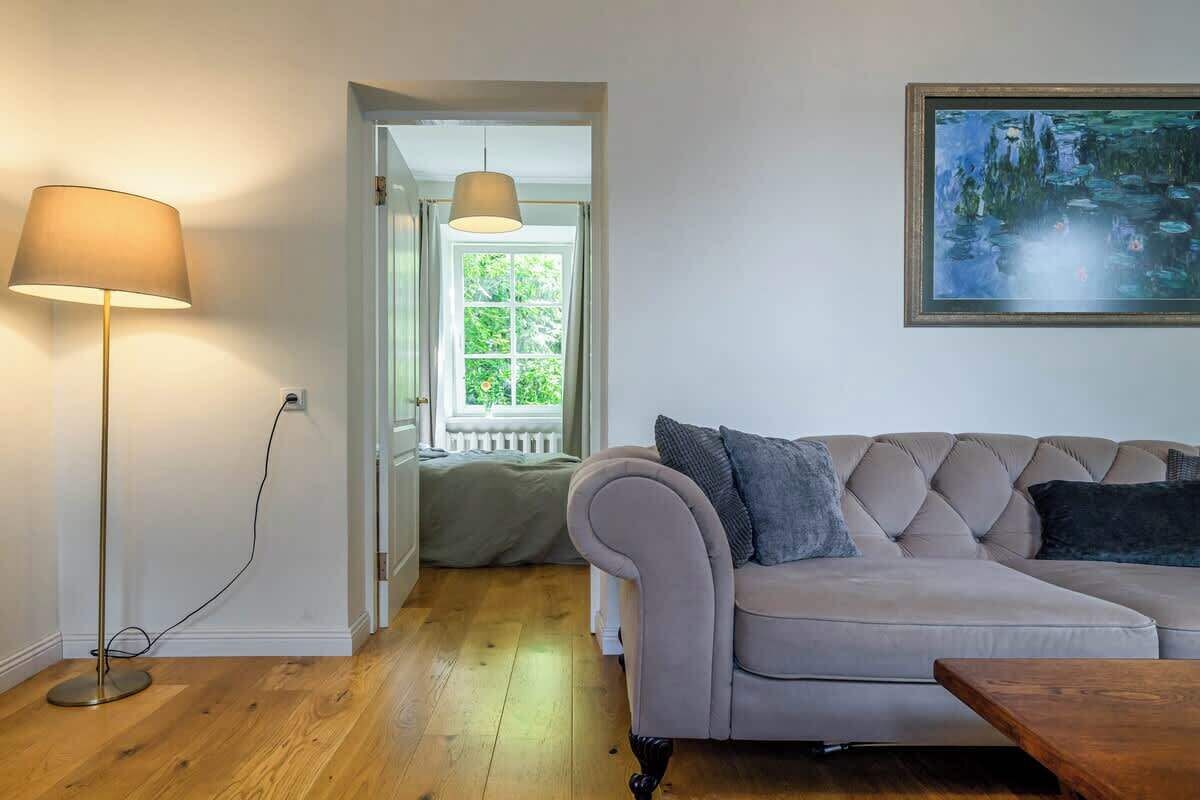 Een woonkamer met een beige bank, een vloerlamp en een schilderij aan de muur.