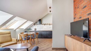 Un espace de vie moderne comprenant un coin repas, un téléviseur posé sur un meuble en bois et une cuisine en arrière-plan.