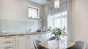 Eine moderne Küche mit weißen Schränken, einer Granit-Arbeitsplatte und einem Essbereich mit einem Glastisch und grauen Polsterstühlen.
