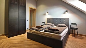 A bedroom with a large bed, two wall-mounted lights, a dark wardrobe, and a skylight.