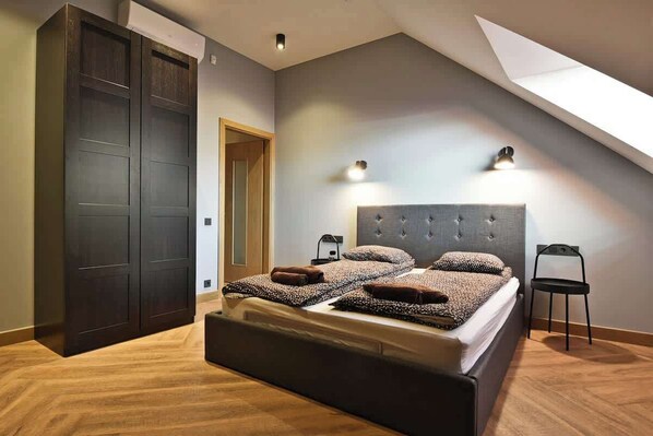 Un dormitorio con una cama grande, dos luces empotradas, un armario oscuro y un tragaluz.