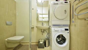 A compact bathroom with a toilet, sink, and stacked washer and dryer.