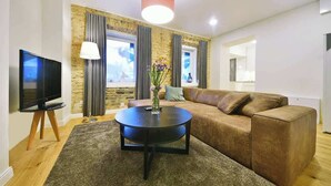 Ein modernes Wohnzimmer mit einem braunen Ledersofa, einem runden schwarzen Couchtisch, einem Flachbildfernseher auf einem Holzboden und einer Wand mit Steinverkleidung.