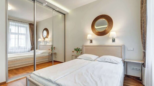 A modern hotel room with a large bed, a mirror, two bedside lamps, and a small table with a lamp. - Zemaitijos Versatile 12ppl Triplex (Vilnius)