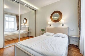 Quarto de hotel moderno com uma cama grande, um espelho, duas luminárias de cabeceira e uma pequena mesa com uma luminária.