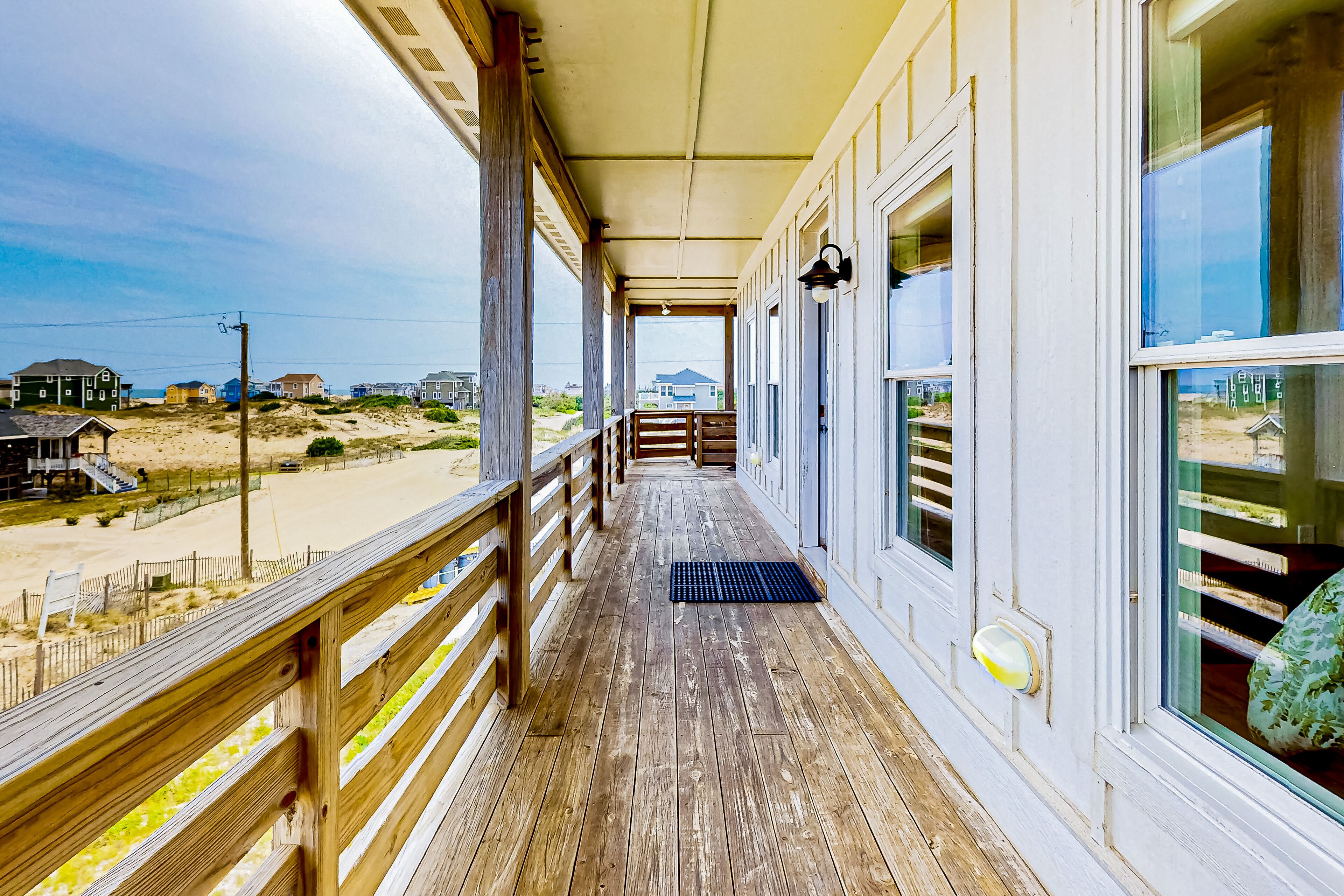 A wooden deck with a view of the beach and houses in the distance.