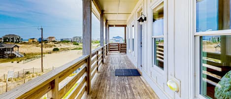 A wooden deck with a view of the beach and houses in the distance.