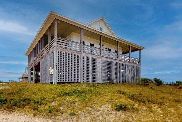 A coastal house with a balcony, a covered porch, and a fenced front yard. - 3BR 4x4 ocean-view & large deck (Corolla)