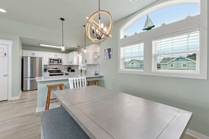 A modern kitchen with a central island, stainless steel appliances, and a view of houses through large windows.