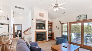 Amplia sala de estar con chimenea, televisor grande y balcón con vistas al exterior.