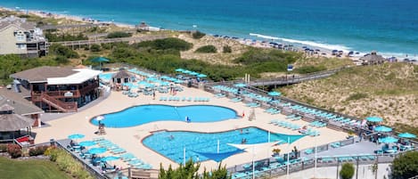 A resort with a large pool area, multiple lounge chairs, and a beach view.