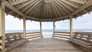A wooden pier leading to a beach with a gazebo structure at the end.