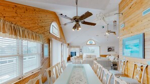 A dining area with a long table, white chairs, and a ceiling fan.