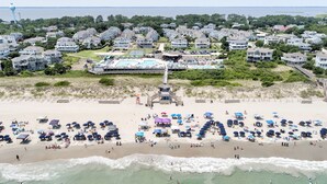 A beach with umbrellas and people, a lifeguard tower, and houses in the background.