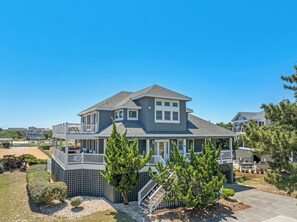 A two-story house with a covered porch, a fenced yard, and a clear blue sky.