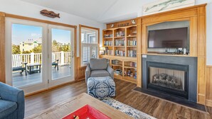 A living room with a fireplace, bookshelves, and a view of the outside deck.