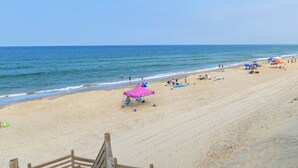 A beach with a wooden staircase leading down to the sand, a pink umbrella, and people relaxing.