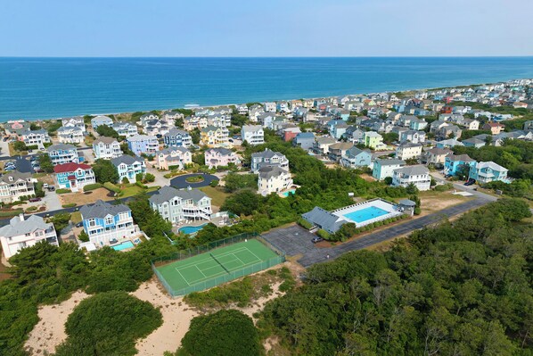 An aerial view of a coastal residential area with houses, a tennis court, and a swimming pool. - Corolla Retreat | Walk to Beach & Amenities (Corolla)