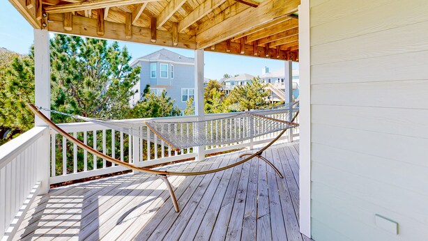 Une terrasse en bois avec un hamac, des balustrades blanches et une vue sur des maisons et des arbres.