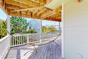 Eine Holzterrasse mit einer Hängematte, weißen Geländern und Blick auf Häuser und Bäume.