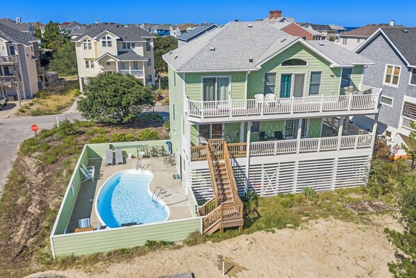 A two-story house with a swimming pool, a balcony, and a sandy beach area.