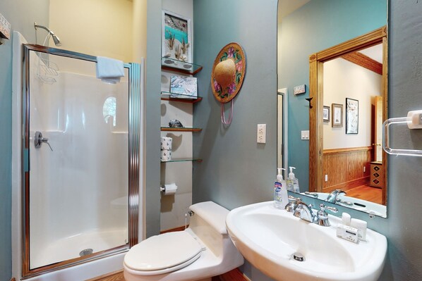 A bathroom with a glass-enclosed shower, a white toilet, a sink with a mirror, and shelves with toiletries. - Walk to Beach 4BR Dog Friendly | Hot Tub (Corolla)