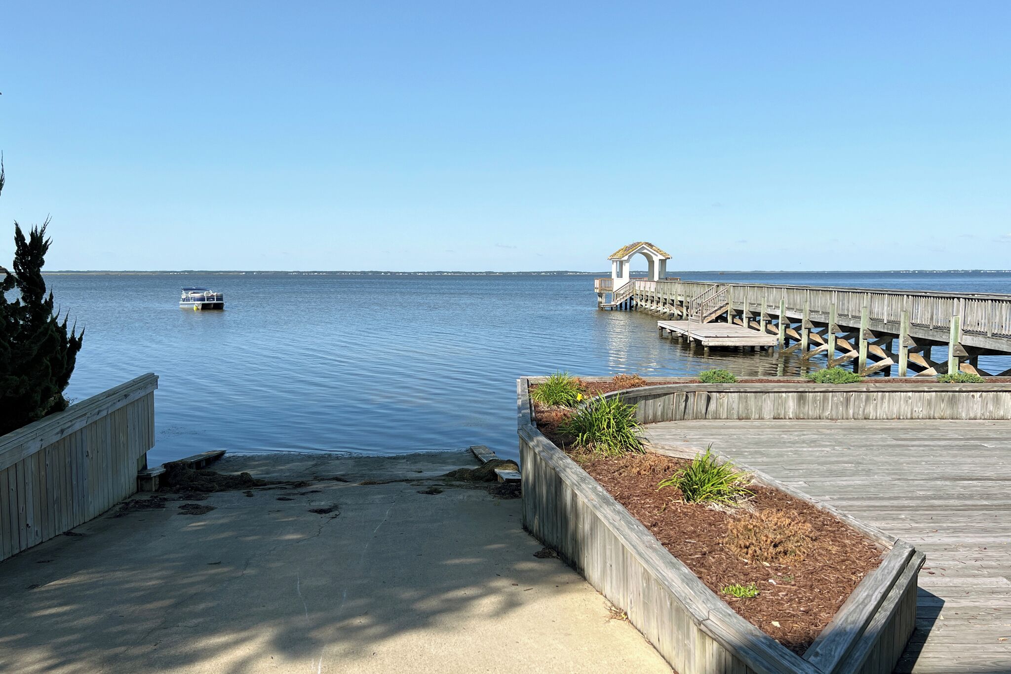 A wooden pier extending into calm waters with a small boat and a gazebo structure.