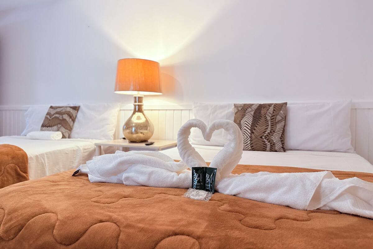 A hotel room with two beds, a lamp, and a heart-shaped towel arrangement on the bed.