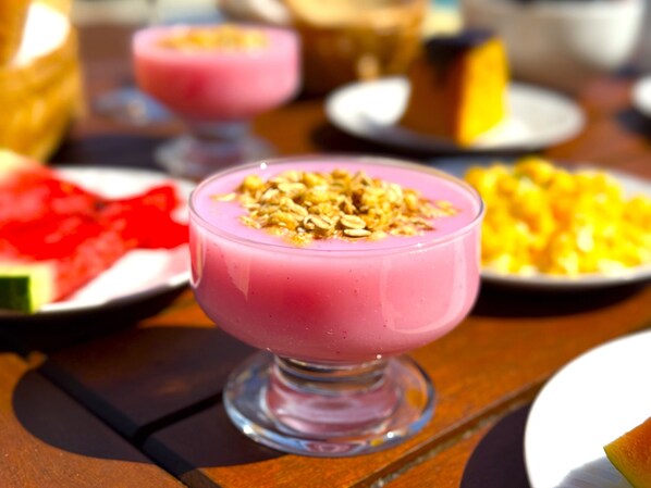 Een desserttafel met een roze smoothie, belegd met granola, omringd door diverse andere gerechten.