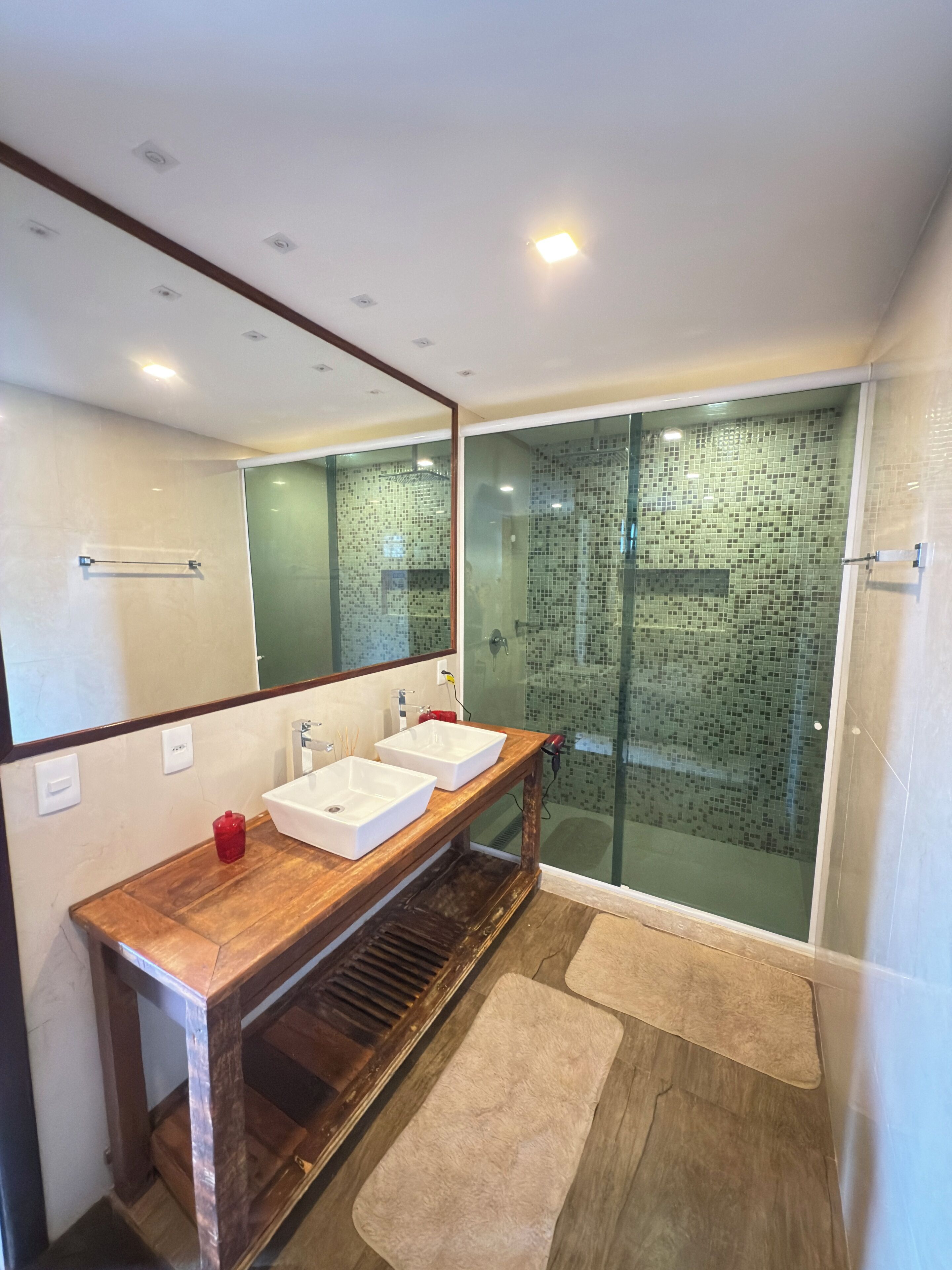 A modern bathroom with two sinks, a wooden vanity, a glass shower enclosure, and a large mirror.