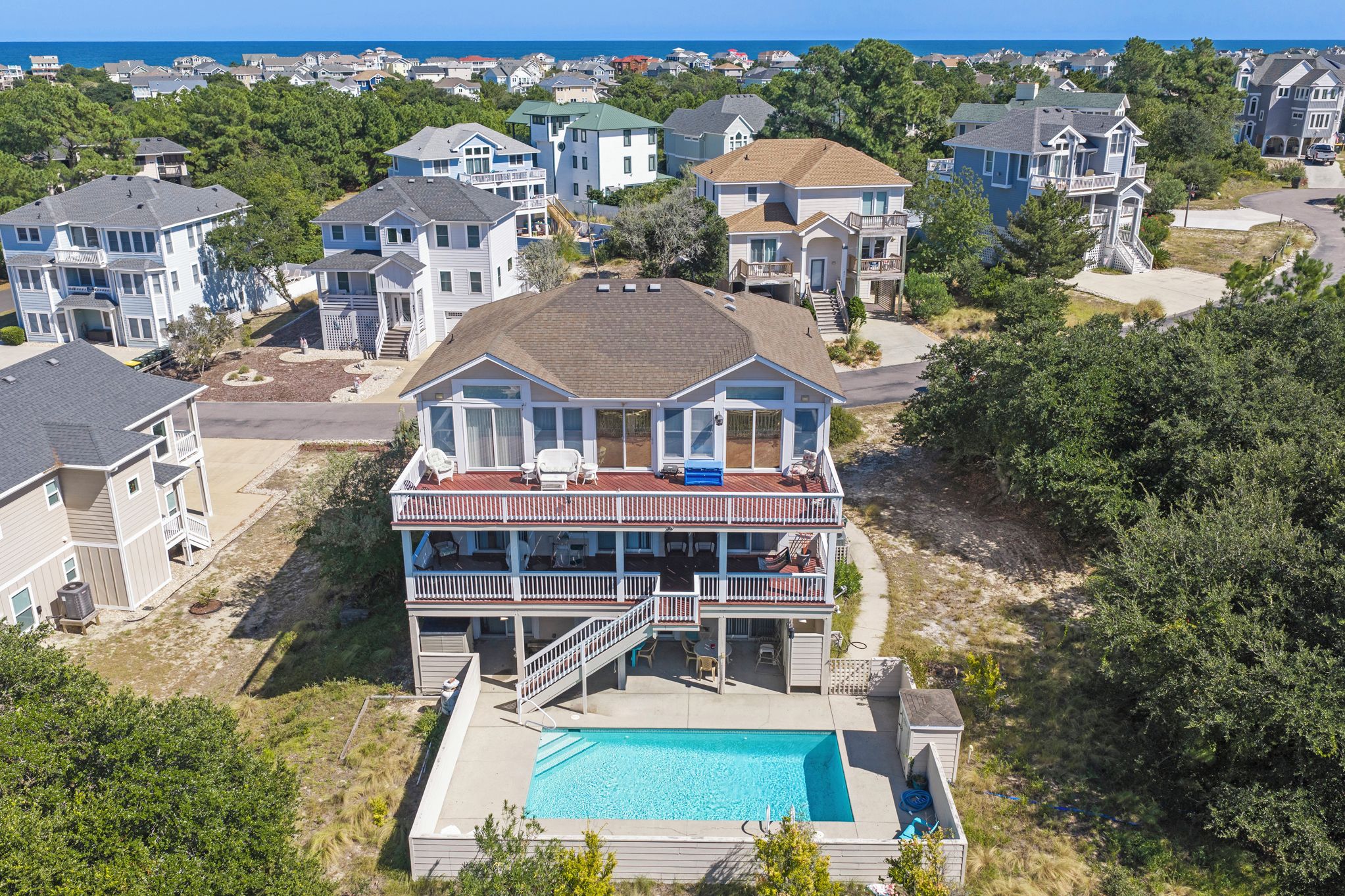 A two-story house with a front deck, a swimming pool, and a view of the ocean.