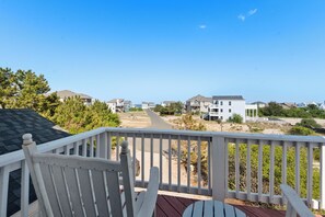 A wooden deck with a white railing, a white chair, and a view of a residential area with houses and a clear sky.