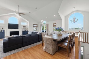 A spacious living room with a large sofa, dining table, and chairs, a fireplace, and a television.
