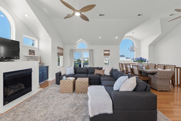 A spacious living area with a large sofa, a fireplace, a dining table with chairs, and a ceiling fan.