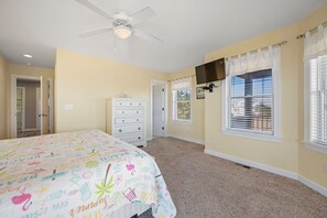 A bedroom with a bed, dresser, ceiling fan, and windows with blinds.