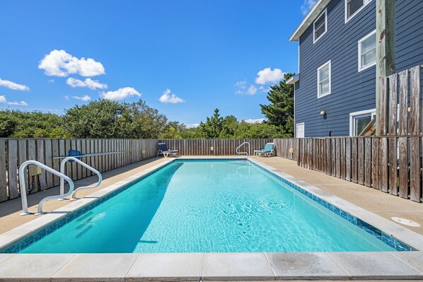 A rectangular swimming pool with a wooden deck, two lounge chairs, and a wooden fence.