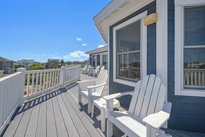 A wooden deck with white chairs, a white railing, and a view of neighboring houses.
