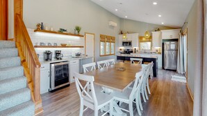 A modern kitchen with white cabinetry, a wooden dining table, and a staircase.