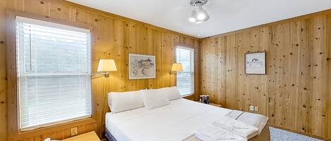 A neatly arranged bedroom with a large bed, two bedside lamps, and wooden paneling.
