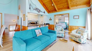 Een ruime woonkamer met een blauwe bank, een houten plafond en een keuken die zichtbaar is door een open doorgang.