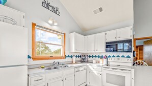 A kitchen with white cabinets, a window, a stove, and a dishwasher.
