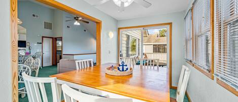 A dining area with a wooden table and white chairs, a ceiling fan, and a view through a glass door to the outside.