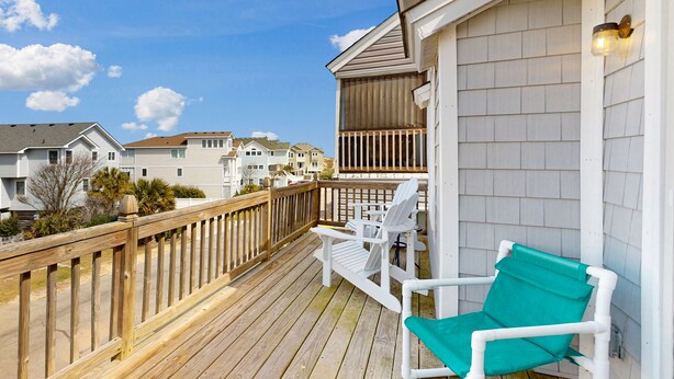 A wooden deck with white chairs and a green cushion, overlooking a residential area with houses. - 3BR townhome by the beach with pool & pickleball (Corolla)