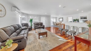 Un salon moderne avec un canapé en cuir marron, une table basse en verre et un coin repas avec des chaises en métal.