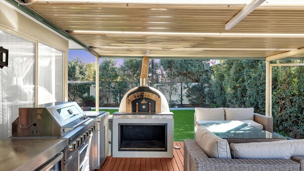 Une cuisine extérieure équipée d’un barbecue, d’un four et d’un espace détente.