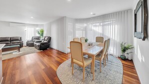 Un salon moderne comprenant un coin repas, un plancher en bois et une grande fenêtre agrémentée de rideaux légers.