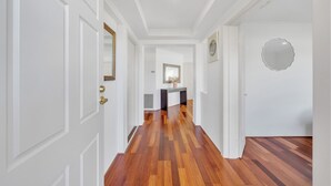 Un couloir aux murs blancs, doté d’un plancher en bois et agrémenté d’une console centrale sur laquelle sont disposés un miroir et des objets décoratifs.