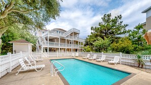 A swimming pool with white lounge chairs and a white fence.