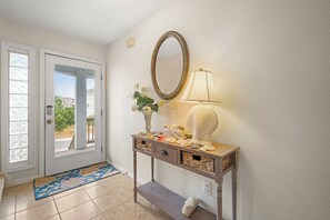 A hallway with a door, a console table with decorative items, a mirror, and a lamp.