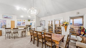 Une cuisine spacieuse avec un coin repas, comprenant une grande table et des chaises en bois, un luminaire suspendu et une vue à travers la porte vitrée.
